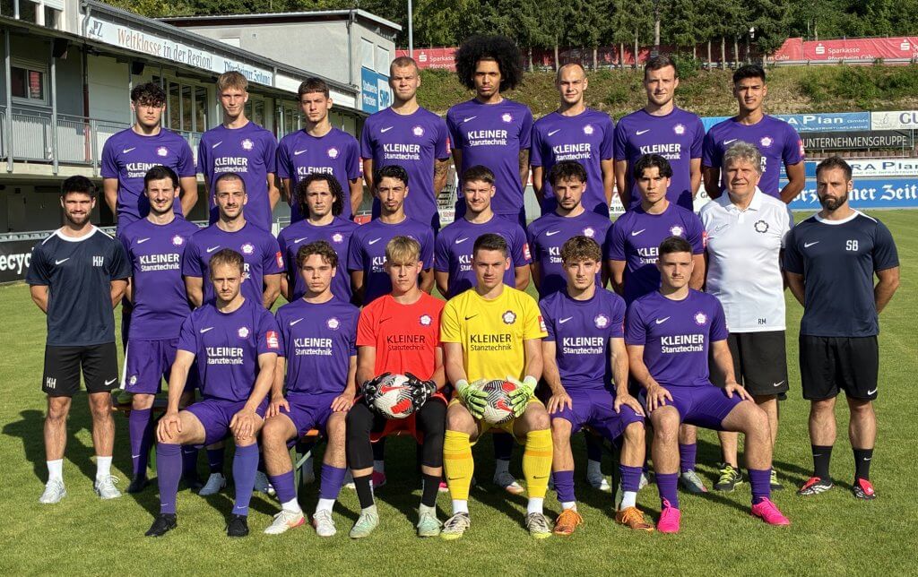 Eine Fußballmannschaft in lila Trikots mit zwei Trainern und zwei Torhütern sitzt und steht draußen in Reihen auf dem Rasen