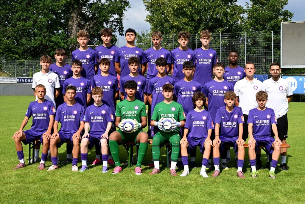 Eine Jungenfußballmannschaft steht draußen in lila Trikots; vorne halten zwei Spieler einen Fußball in den Händen