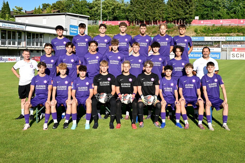 Eine Jugendmannschaft in lila Trikots posiert zusammen mit den Trainern am Spielfeldrand für ein Gruppenfoto auf dem Fußballplatz