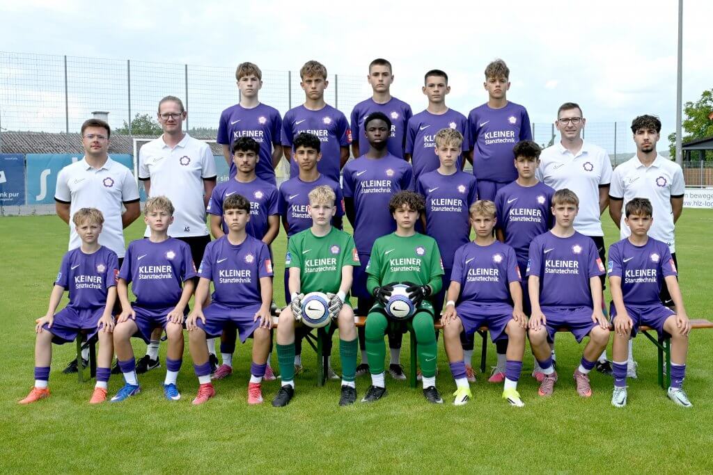 Eine Jugendfußballmannschaft in lila Trikots posiert mit ihren Trainern für ein Gruppenfoto auf einem Rasenplatz