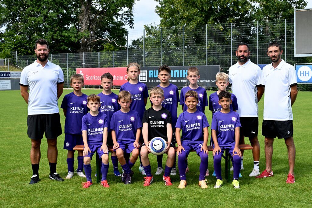 Eine Jugendfußballmannschaft in lila Trikots steht mit drei Trainern und einem Ball auf dem Spielfeld